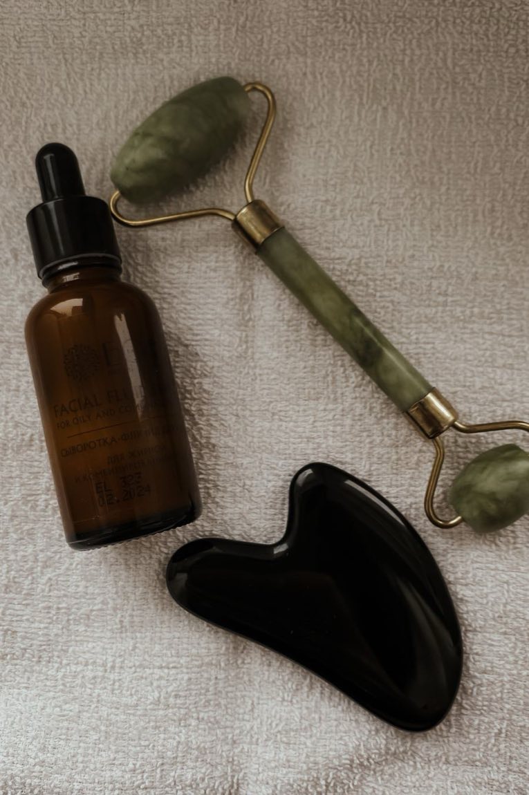 Jade roller, gua sha stone, and an amber glass dropper bottle on a waffle-weave towel