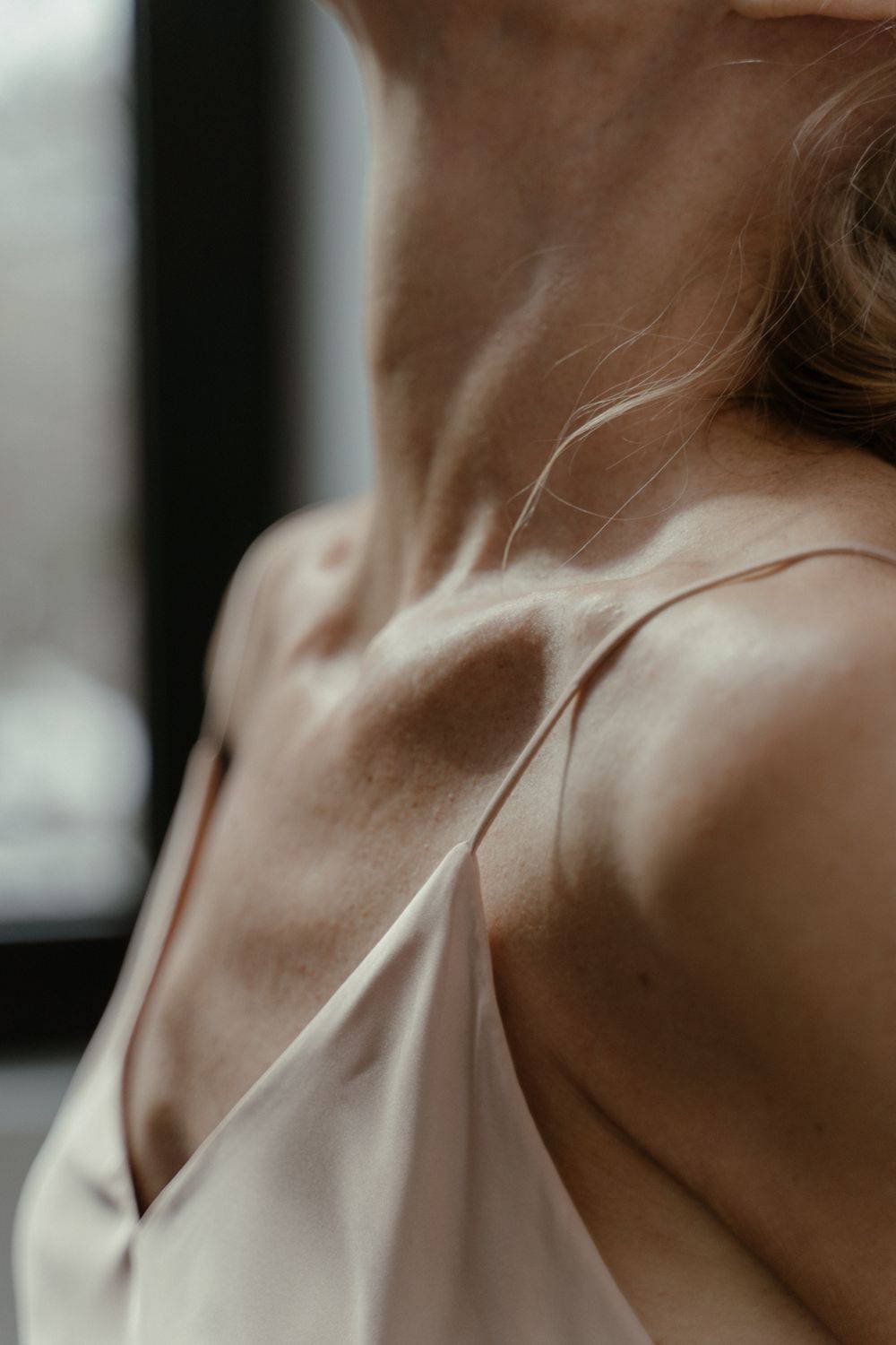 Neck and collarbone in soft window light, skin texture visible and unretouched