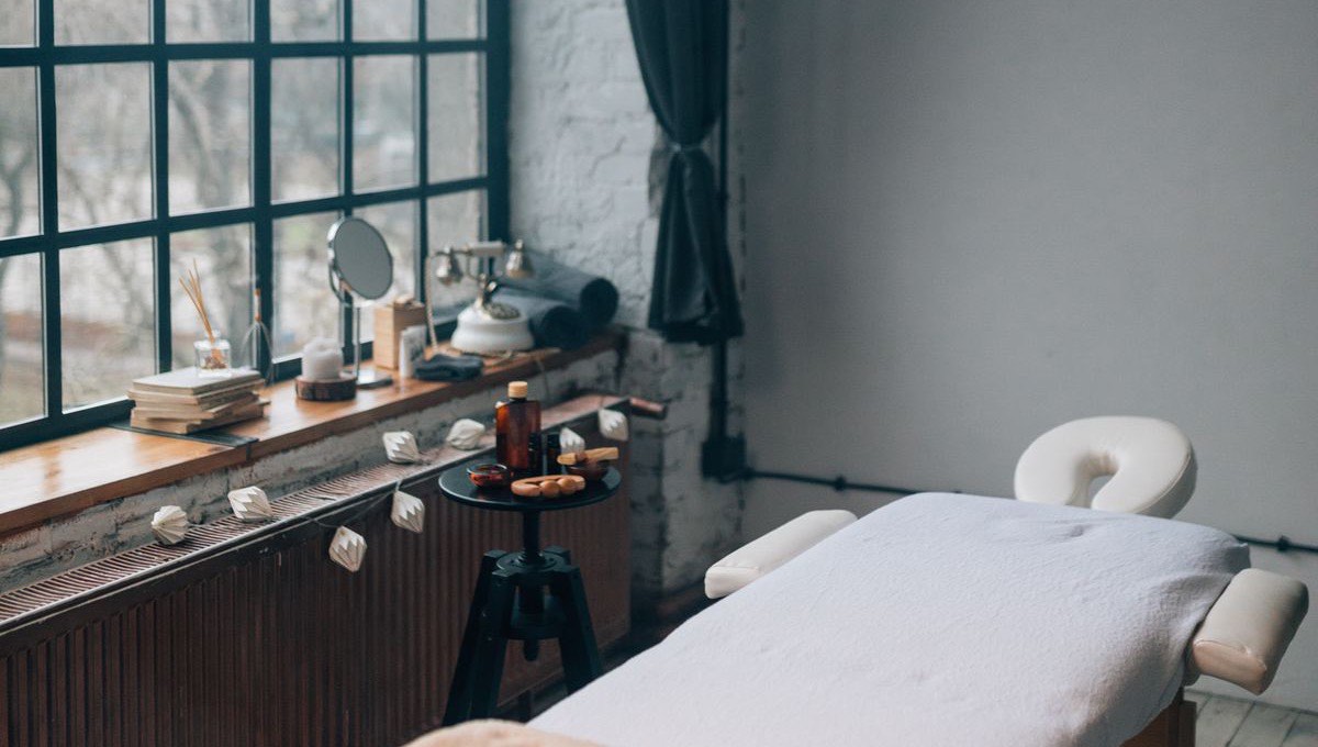 A treatment bed under a tall steel-framed window, amber glass on the ledge, grey morning light