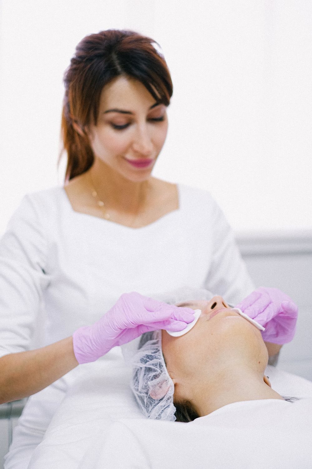 A practitioner in white working through a facial treatment, patient reclined and at ease